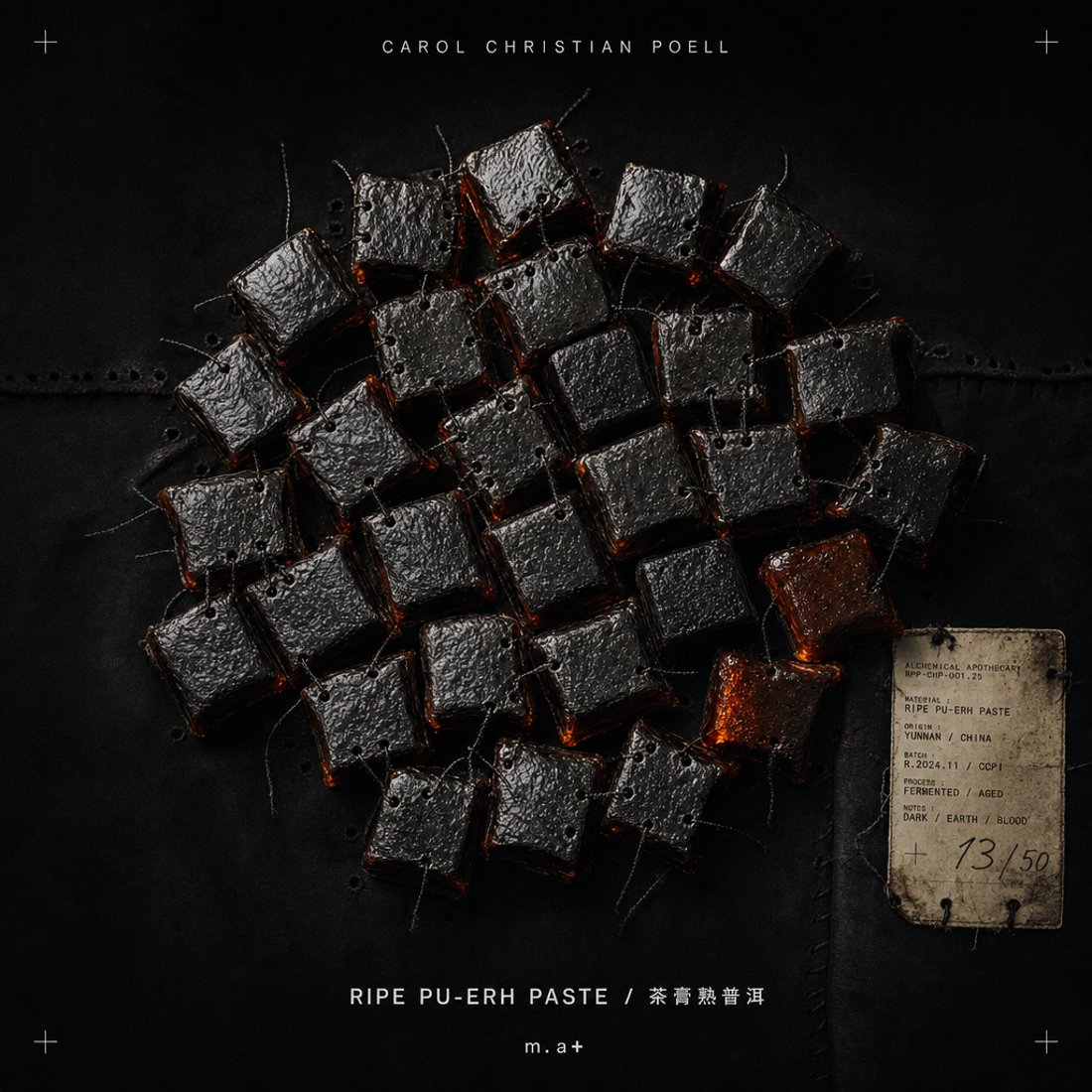 Ripe pu-erh paste cubes on black waxed cloth with loose threads across them and a stained paper tag hand-numbered thirteen of fifty